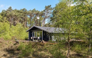 A cabin with a large glass door, surrounded by trees and a deck with outdoor furniture.