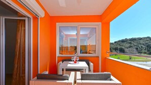 A balcony with a table and chairs, a window with orange walls, and a view of a green landscape.