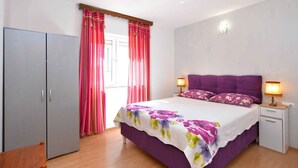 A bedroom with a bed, curtains, a wardrobe, a bedside table with a lamp, and a nightstand.