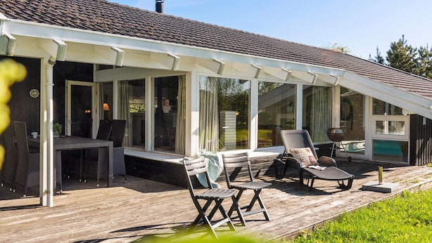 A covered outdoor seating area with wooden deck, chairs, and a grill. - 3 bedroom beautiful home in Hjørring (Hjørring)