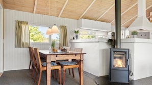 A cozy dining area with a wooden table and wicker chairs, a built-in wood stove, and a window with curtains. - 3 bedroom beautiful home in Hjørring (Hjørring)