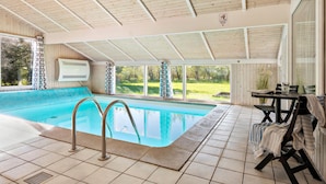 An indoor swimming pool with a view of a green landscape, a table with chairs, and a ceiling with wooden beams. - 3 bedroom beautiful home in Hjørring (Hjørring)