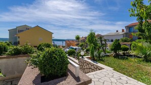 A residential area with a yellow house, a stone wall, and a view of the sea. - Holiday apartment with garden and barbecue (Crikvenica)