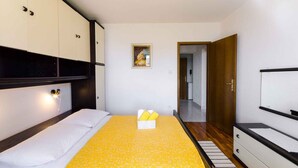 A bedroom with a bed, a bedside table, a wall-mounted TV, a door, and a hallway. - Holiday apartment with garden and barbecue (Crikvenica)