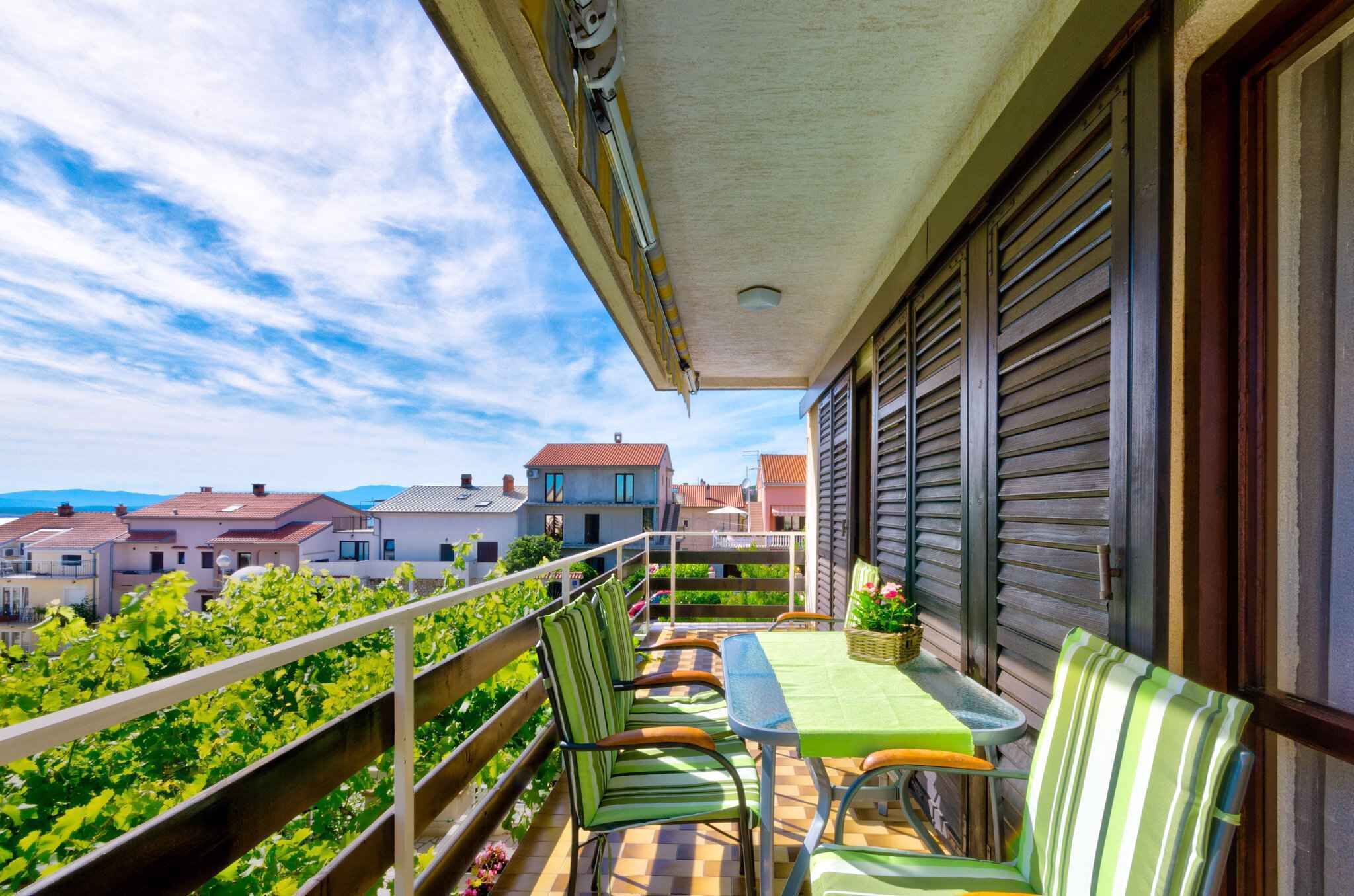 Un balcone con tavolo e sedie, affaccia su una zona residenziale con case e cielo sereno.
