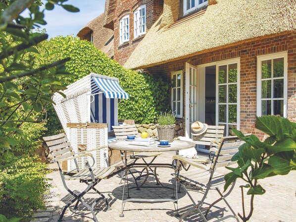 A patio with a striped beach chair, a round table, and a thatched-roof structure.