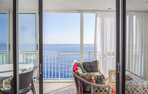 Uma varanda com vista para o oceano, uma cadeira de vime com almofadas e uma mesa com cadeiras.