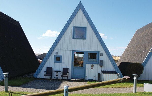 Un bâtiment triangulaire avec une porte et des fenêtres bleues, une petite table et deux chaises à l’extérieur.