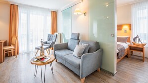 Habitación de hotel moderna con un sofá gris, una mesa de centro de madera y una cama con cabecero de madera.