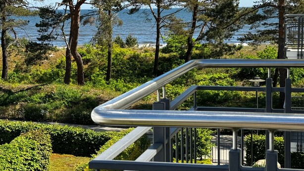 Barandilla metálica con vistas a un jardín ajardinado, árboles y el mar.