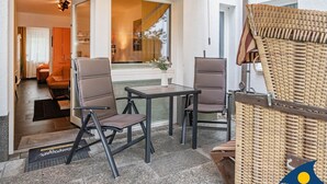 A modern outdoor seating area with two chairs and a table, a wicker chair, and a door leading to an interior space. - Dünenhaus Christa Apartment 04 - DHC 04 (Heringsdorf)