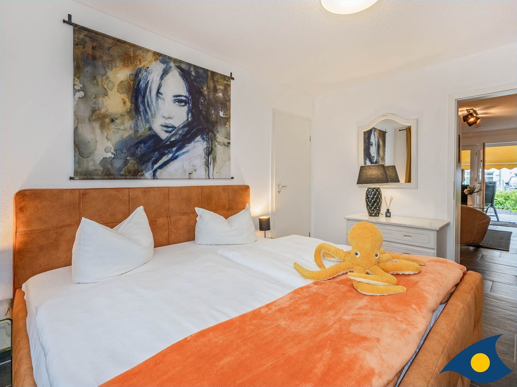 A hotel room with a large bed, a painting on the wall, a desk with a lamp, and a view of the outside.