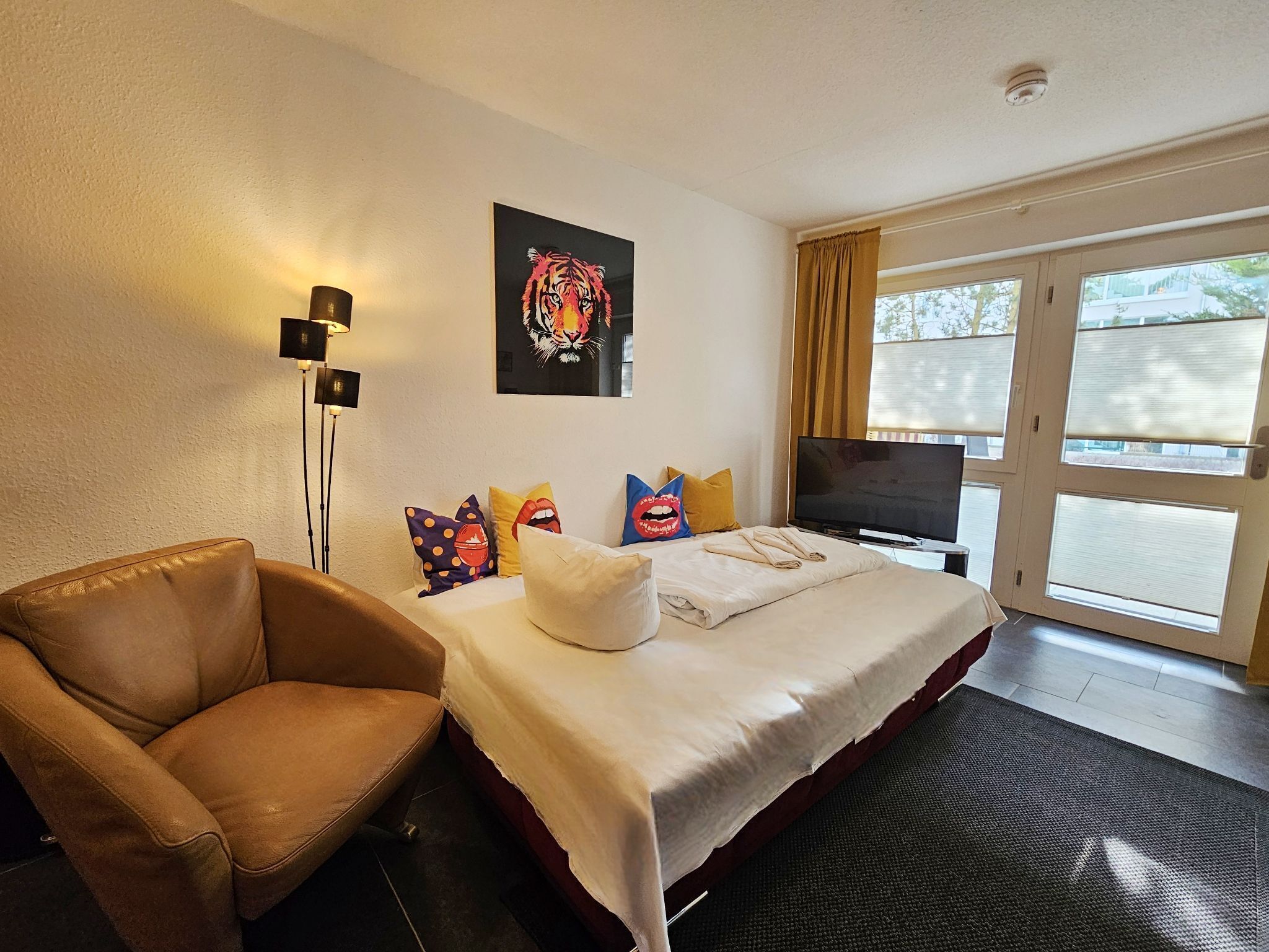 A hotel room with a bed, a chair, a TV, and a painting on the wall.