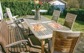 Ein Holzes-Esstisch im Freien mit passenden Stühlen, einer Metallkanne und einem kleinen Tisch.
