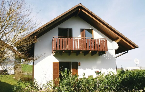 Ein zweistöckiges Haus mit Balkon, Satellitenschüssel und kleinem Garten.