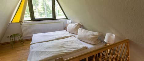 Una habitación pequeña y triangular con cama, mesita de noche, lámpara y radiador.