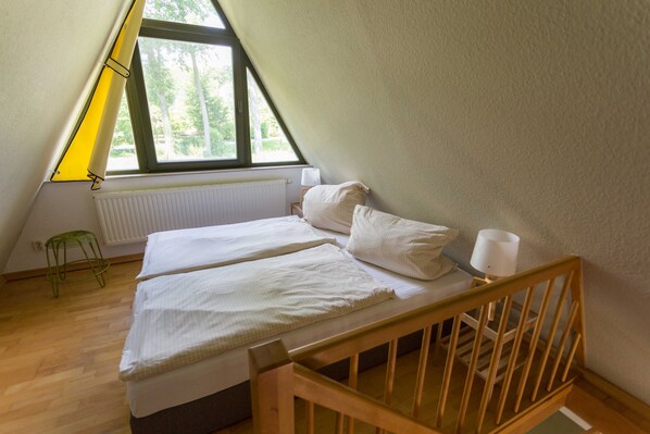 A small, triangular room with a bed, a nightstand, a lamp, and a radiator.