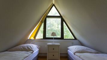 Une chambre avec deux lits, une table de chevet, une lampe et une fenêtre donnant sur des arbres.