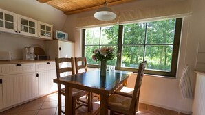 A kitchen with wooden cabinets, a dining table with chairs, a window with a view of trees, and a hanging light fixture.