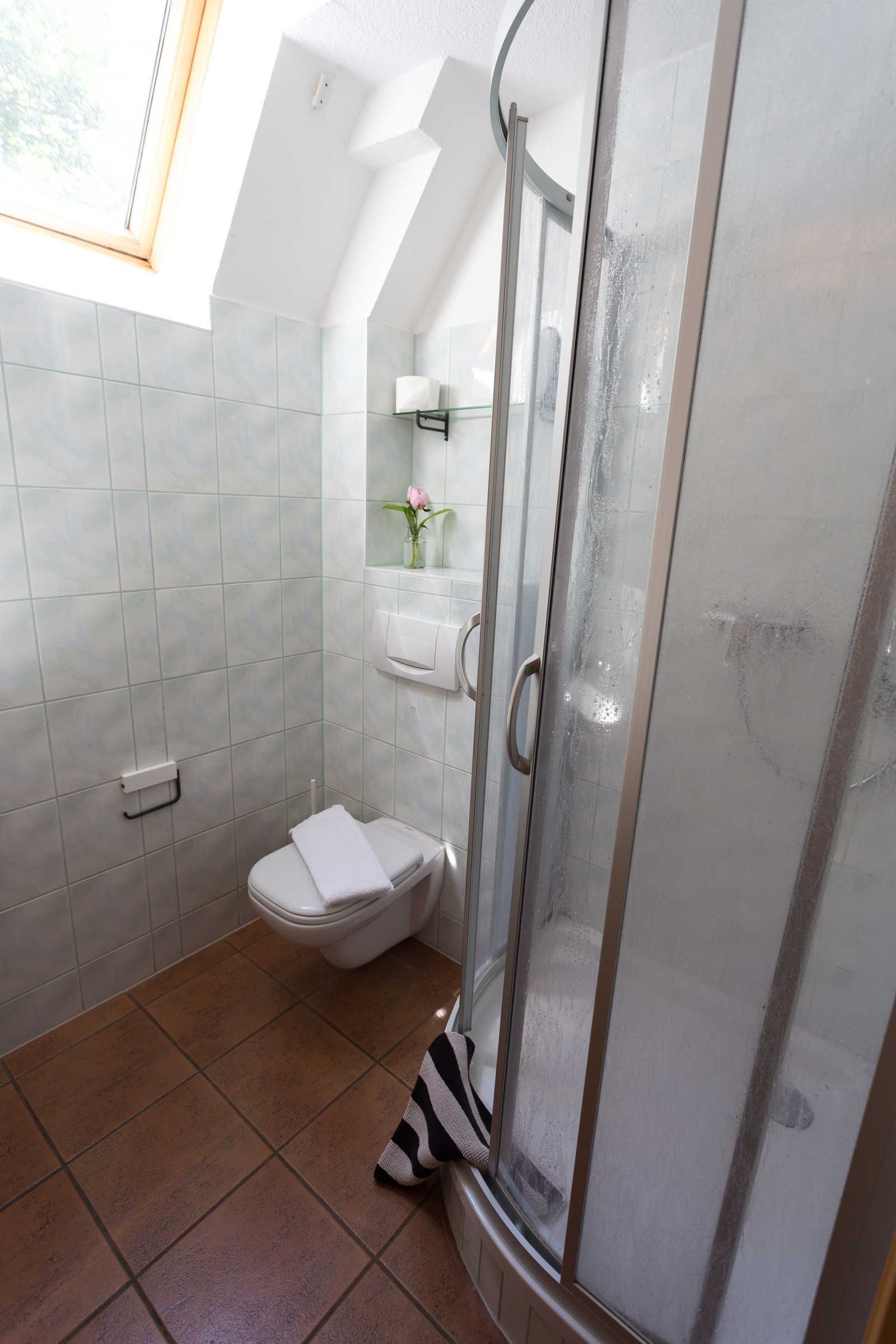 Une salle de bain avec une douche à parois de verre, des toilettes et une petite fenêtre.