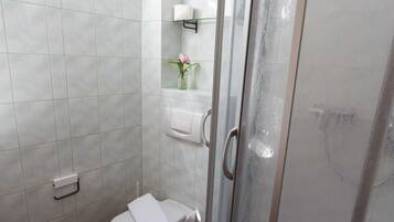 Une salle de bain avec une douche à parois de verre, des toilettes et une petite fenêtre.