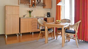 A compact kitchen with wooden cabinets, a built-in oven, and a dining area with wicker chairs and a table. - FEWO 07 - Villa Celia Sellin (Sellin)