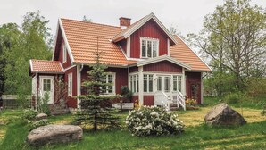 A red wooden house with a sloped roof, a white porch, and a garden with rocks and flowers. - 2 bedroom amazing home in Markaryd (Markaryd)
