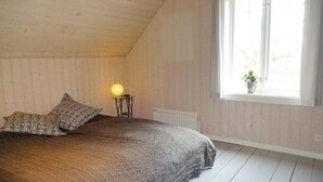 A bedroom with a sloped ceiling, a bed with patterned pillows, a bedside table with a lamp, and a window with a view of greenery. - 2 bedroom amazing home in Markaryd (Markaryd)