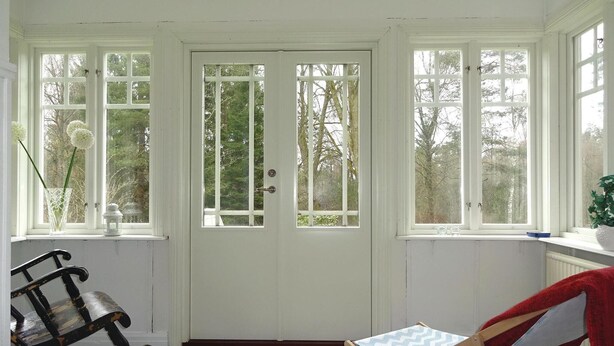 A room with a white door, two windows, a rocking chair, a small table, and a red chair. - 2 bedroom amazing home in Markaryd (Markaryd)