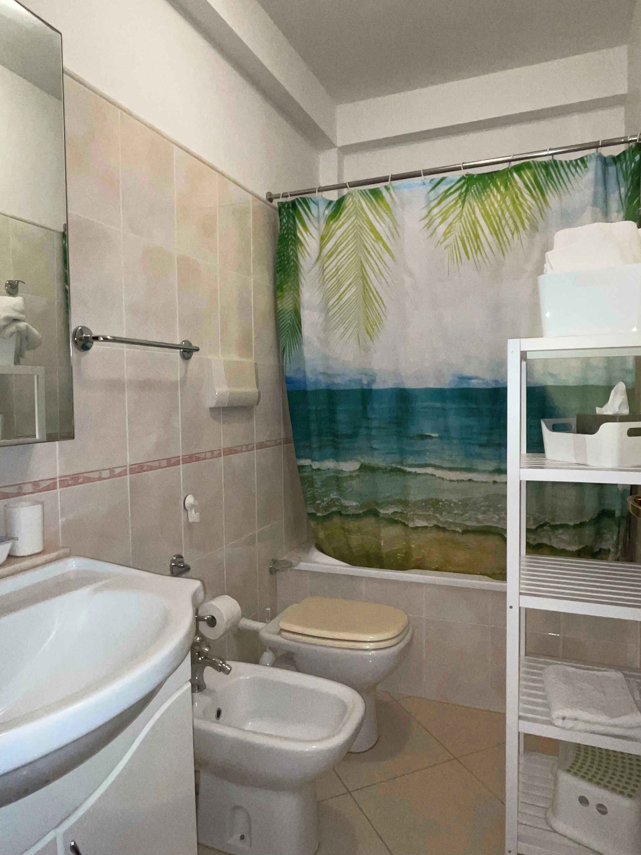 Un baño con lavamanos, bidé, inodoro y cortina de ducha con una escena de playa.