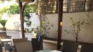 Eine Terrasse im Freien mit Tisch und Stühlen, umgeben von Blumentöpfen und einer Pergola.