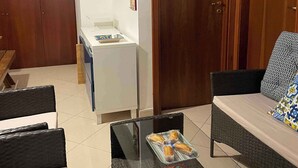 Ein Wohnzimmer mit einer Couch, einem Couchtisch mit Zeitschriften, einem kleinen Tisch mit einer Brottüte und einer Holztreppe sowie einer Holztür.