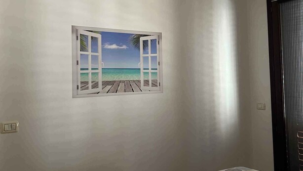 Ein Schlafzimmer mit einem Bett, einer Klimaanlage, einem an der Wand hängenden Bild von einem Strand und einer Tür.