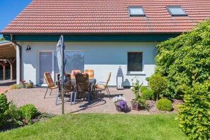 A house with a red tiled roof, a covered patio with outdoor furniture, and a garden with various plants.