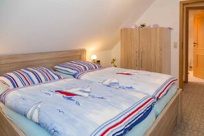 A bedroom with a bed, a wooden wardrobe, and a nightstand with a lamp.