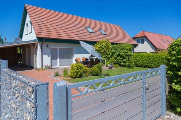 A residential property with a red-tiled roof, a covered patio with outdoor furniture, and a gated entrance.