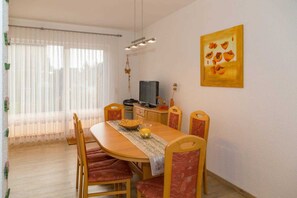 A dining area with a wooden table, red upholstered chairs, a television, and a painting on the wall.
