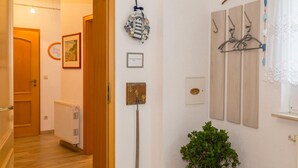 Corredor com porta de madeira, radiador, placa de boas-vindas, quadro emoldurado, cabideiro e um vaso com planta.