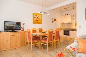 A compact living space with a dining area, a kitchenette, and a television on a wooden cabinet.