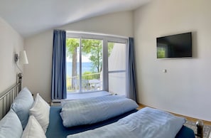 Ein Hotelzimmer mit Bett, Fernseher, Fenster mit Vorhängen und Meerblick.