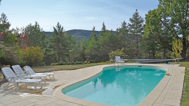 Una piscina rectangular con borde de baldosas, rodeada de árboles y vistas a colinas.