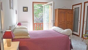 Un dormitorio con cama, mesita de noche, armario de madera y ventana con vista a follaje.