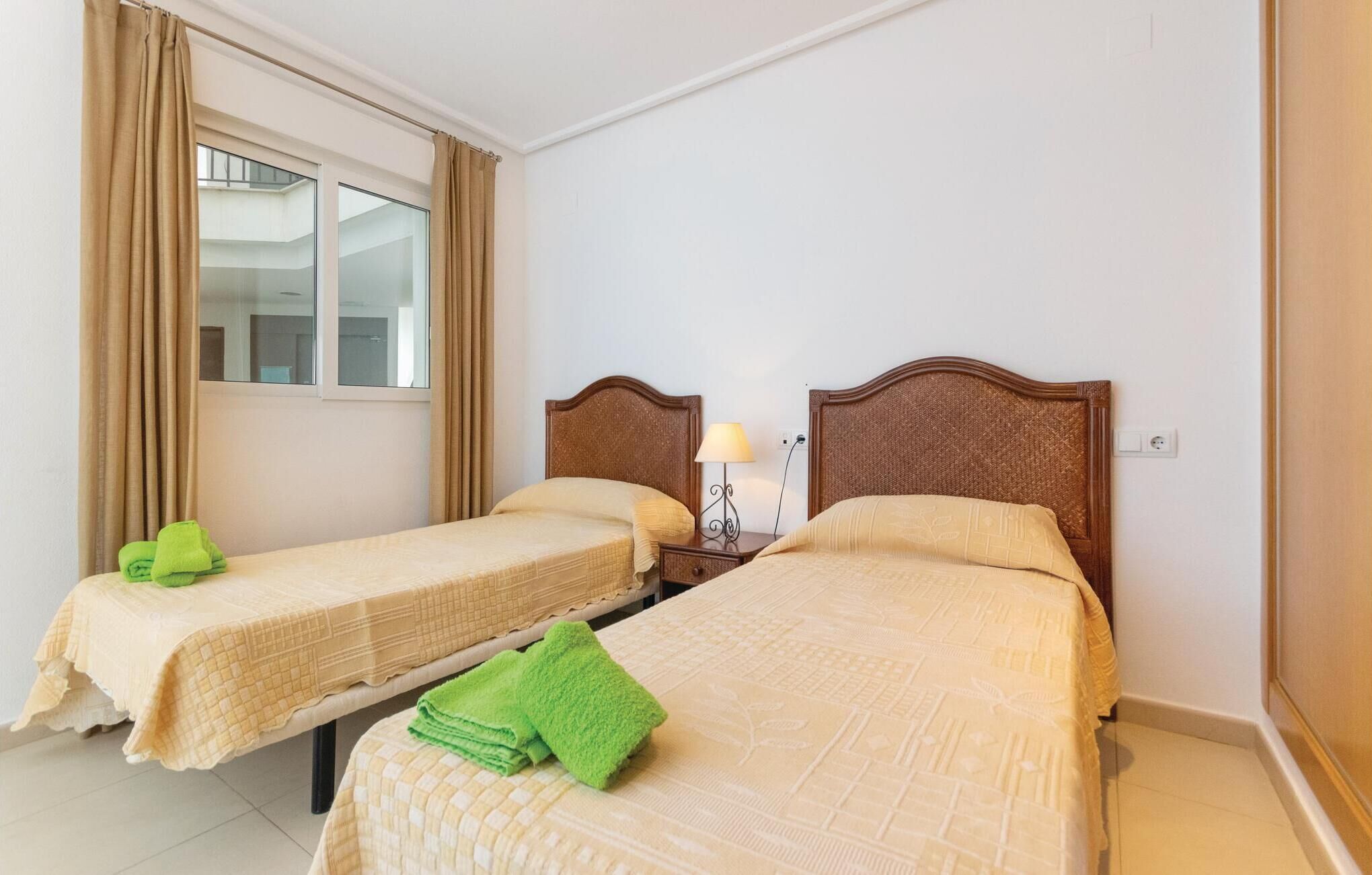 Habitación de hotel con dos camas, una ventana con cortinas, una mesita de noche con lámpara y un enchufe en la pared.