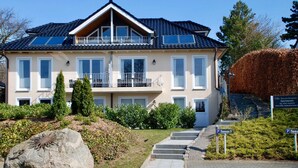 A two-story house with a balcony, solar panels, and a stone sculpture in the garden. - Villa Sun 4, 2-5 P. Terrace - Villa Sun Terrace, Nicole Struck (Neustadt in Holstein)