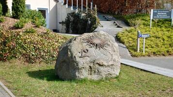 Ein großer Felsen mit Sonnendesign und der Zahl 12, ein Weg zu einem Gebäude und ein Schild für die Villa Sonnenterrasse Apartments.