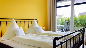 A double bed with white linens and pillows, a black metal frame, and a yellow wall. - Villa Sun 4, 2-5 P. Terrace - Villa Sun Terrace, Nicole Struck (Neustadt in Holstein)