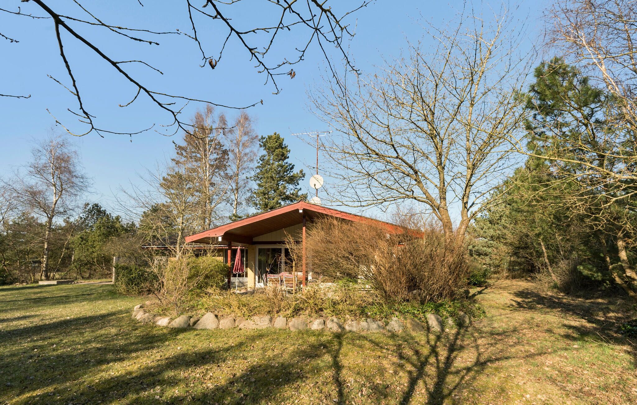 A small, single-story building with a red roof and a satellite dish on top. It is surrounded by trees and has a grassy area in front.