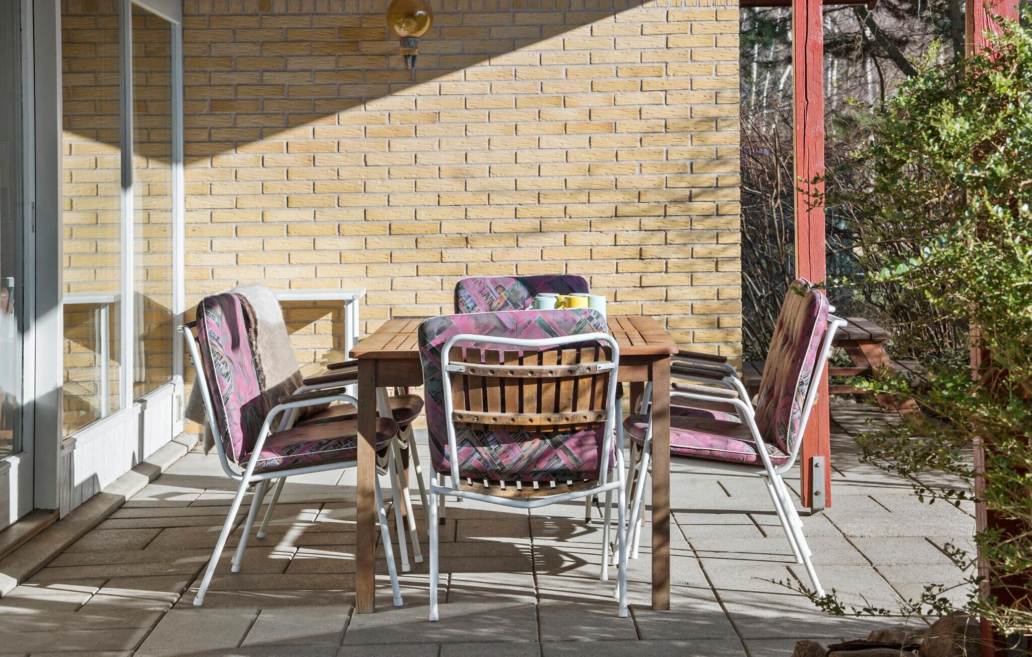 An outdoor patio with a brick wall, a wooden table, and metal chairs.