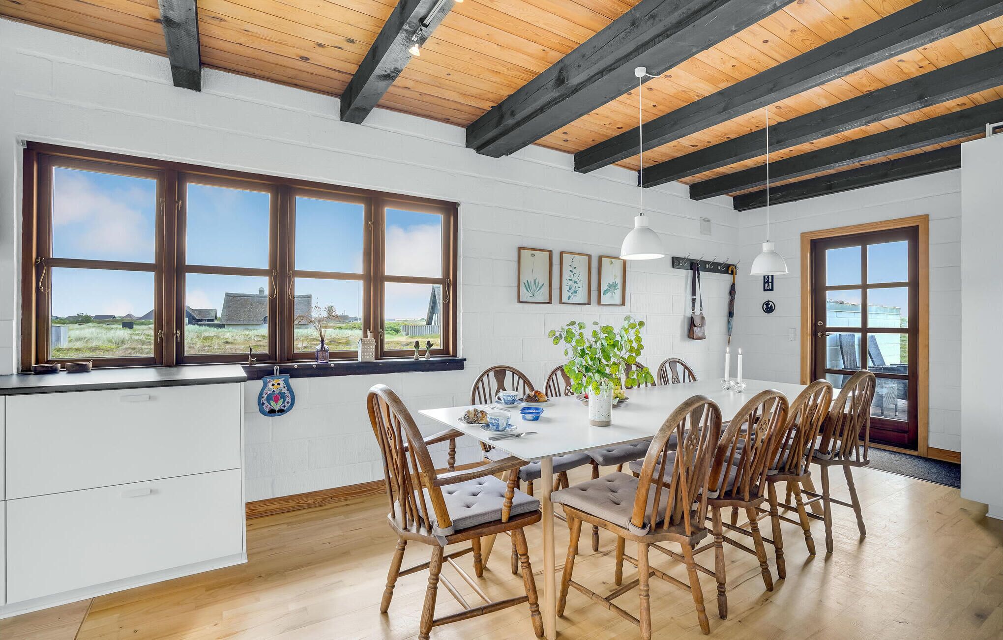 A spacious kitchen with large windows, wooden beams, and a dining area with a white table and wooden chairs.