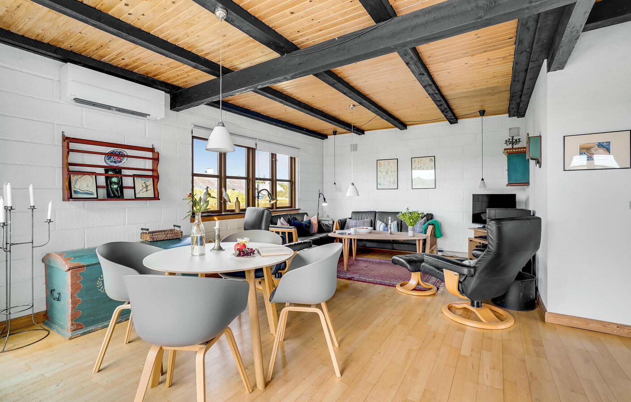 Un salon spacieux avec un plafond haut, des poutres en bois, une grande fenêtre et un coin salon confortable avec un canapé et des fauteuils.